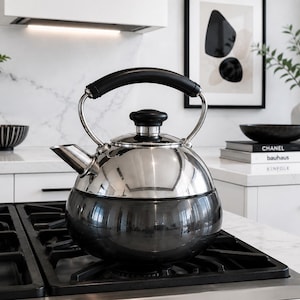 May include: A stovetop tea kettle featuring a polished stainless steel upper section and a dark charcoal grey rounded base. It includes a black handle, a matching black lid knob, and a short spout, all resting on a black metal gas stove grate.