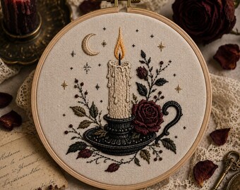 May include: A circular wooden embroidery hoop containing a fabric panel with a stitched design of a lit candle in a black holder, a dark red rose, leafy stems, and a crescent moon with small stars, all rendered in detailed thread work.