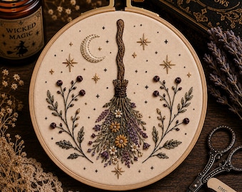 May include: A circular wooden embroidery hoop containing a fabric panel with a hand-stitched design of a broomstick adorned with flowers and lavender. The scene includes a crescent moon, stars, and two symmetrical floral branches on the sides.