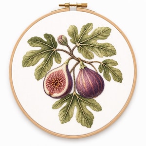 May include: Embroidery hoop featuring a detailed fig design. The artwork showcases two ripe figs, one sliced open to reveal the interior, surrounded by green leaves and a bud. The embroidery is set against a white fabric background.