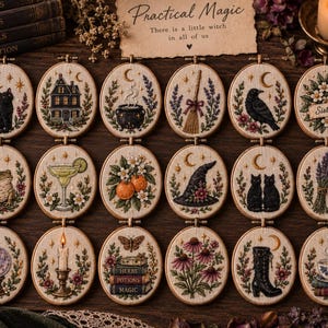 May include: A collection of eighteen oval embroidery hoops featuring detailed needlework designs including a black cat, a house, a cauldron, a broom, a crow, flowers, a frog, a cocktail, oranges, a witch hat, two cats, lavender, a crystal ball, a candle, books, plants, a boot, and a teacup.