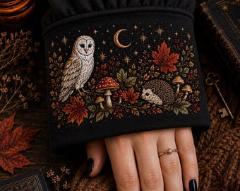 May include: A black long-sleeved garment featuring an embroidered cuff with a detailed nature scene. The design includes a white owl, a hedgehog, red mushrooms, and autumn leaves under a crescent moon and stars, all rendered in warm earth tones.