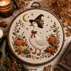 May include: A circular embroidery hoop featuring a white fabric background with a stitched design of a white goose wearing a black witch hat and a brown bow tie. The goose is surrounded by orange pumpkins, green vines, and gold stars.