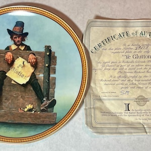 May include: A decorative plate featuring a painting of a man in stocks holding a sign that reads "Ye Glutton". The plate has a gold rim and is accompanied by a certificate of authenticity. The artwork is a historical piece.