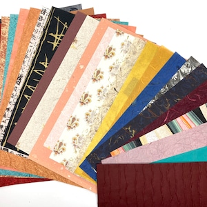 May include: A collection of 20 different patterned papers in various colors, including black, white, brown, blue, red, and green. The papers are arranged in a fan shape, with the top of the fan folded over. The papers are all textured and have a variety of patterns, including floral, geometric, and abstract.