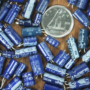 May include: A close-up image of a collection of blue and silver capacitors. The capacitors are various sizes and have different markings, including voltage and capacitance values. Some of the capacitors have the text "TAICON" printed on them.