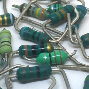 May include: A close-up of a pile of green, black, and brown resistors. The resistors are all bent into a U-shape and have metal leads.