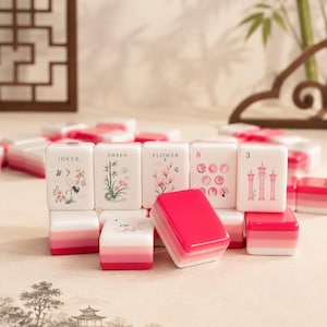 May include: A set of white mahjong tiles featuring pink gradient bases and intricate illustrations. The tiles display various symbols including a crane, bamboo, flowers, the number 8, the number 3, and text labels such as JOKER, GREEN, and FLOWER.