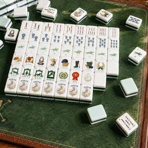 May include: A set of white mahjong tiles featuring equestrian-themed illustrations, including horses, saddles, ribbons, and riding gear. The tiles are arranged in a grid on a green felt surface, with some loose tiles scattered around the main display.