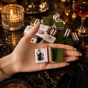 May include: A collection of rectangular mahjong tiles featuring white faces with illustrations of cocktails, oysters, and a woman in a black dress labeled Joker, alongside tiles with solid olive green backs and white and red striped side edges.