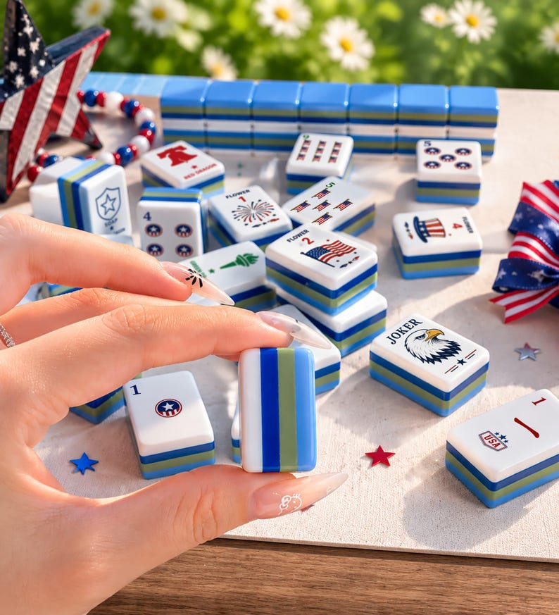 May include: A set of white mahjong tiles featuring patriotic American-themed graphics including eagles, flags, and stars. The tiles have blue and green striped sides and are arranged with a star-shaped decoration and red, white, and blue ribbons.