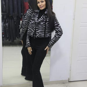 May include: A silver and black zebra-striped jacket with a black turtleneck and black flared trousers. The jacket has a zip closure. The trousers are a solid black colour. The outfit is displayed in front of a mirror.
