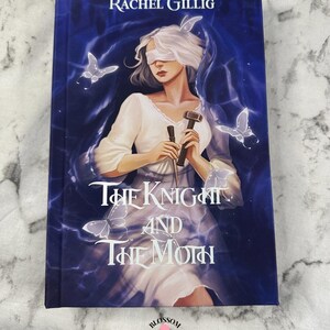 Puede incluir: Portada del libro "The Knight and The Moth" de Rachel Gillig. La imagen muestra a una mujer con los ojos vendados, sosteniendo un martillo y un objeto oscuro, rodeada de mariposas y luz azul.