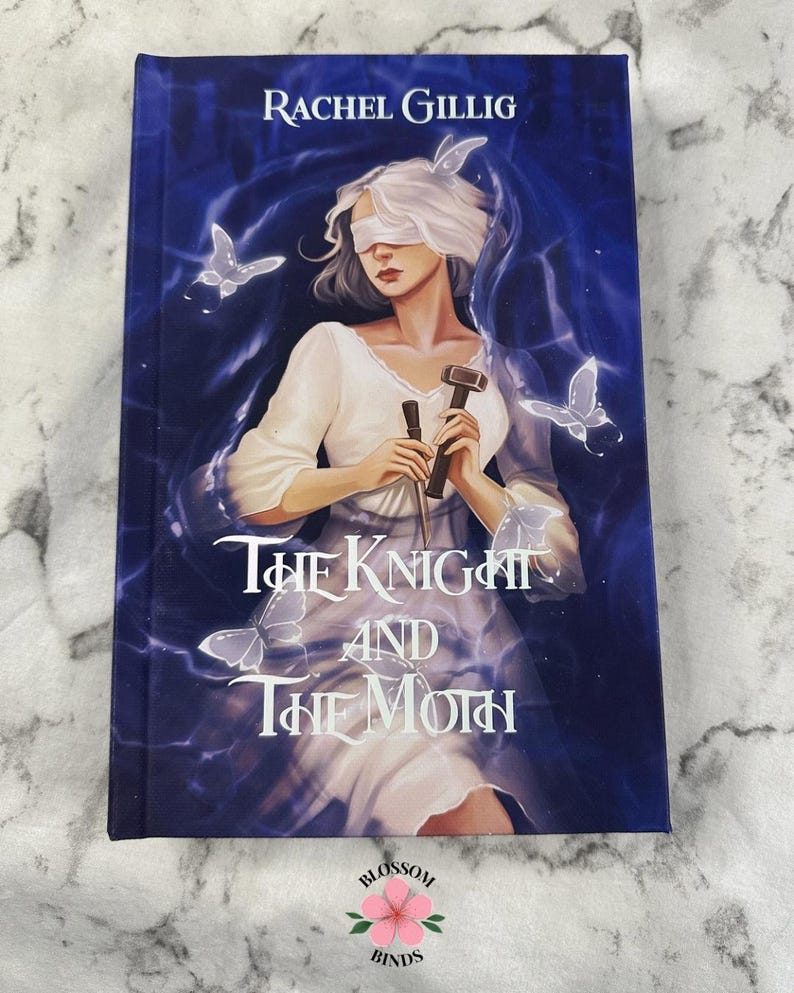 Puede incluir: Portada del libro "The Knight and The Moth" de Rachel Gillig. La imagen muestra a una mujer con los ojos vendados, sosteniendo un martillo y un objeto oscuro, rodeada de mariposas y luz azul.