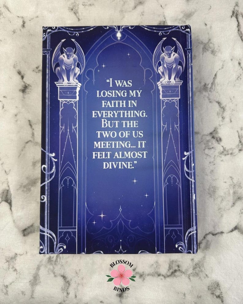 Puede incluir: Una portada de libro con un fondo azul oscuro y detalles en blanco. La portada presenta una cita: "Estaba perdiendo la fe en todo. Pero nosotros dos reuni&eacute;ndonos... se sinti&oacute; casi divino." Dos g&aacute;rgolas se sientan sobre columnas. El logotipo de Blossom Binds est&aacute; en la parte inferior.