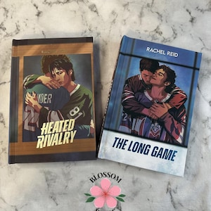 Puede incluir: Dos libros con ilustraciones de hombres con camisetas de hockey. Un libro se titula "Heated Rivalry" y el otro "The Long Game". El nombre del autor, Rachel Reid, está impreso en la parte superior de cada libro.