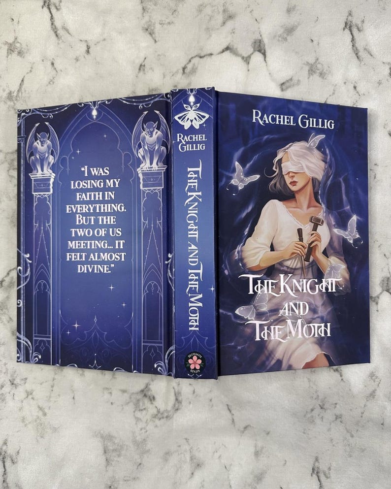 Puede incluir: Libro de tapa dura titulado "The Knight and The Moth" de Rachel Gillig. La portada presenta a una mujer con los ojos vendados, sosteniendo herramientas y mariposas. El lomo y la contraportada son de color azul oscuro con elementos decorativos y texto.