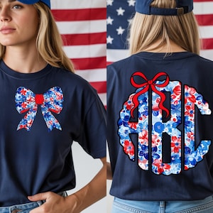 Può includere: T-shirt blu navy con un design a fiocco patriottico con motivi floreali rossi, bianchi e blu. La parte posteriore della maglietta presenta un monogramma con un fiocco rosso e accenti floreali. Stile casual e confortevole.