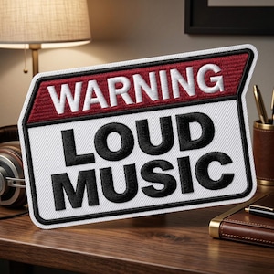 May include: Embroidered patch with the words "WARNING LOUD MUSIC" in black and white. The top section is red with white text. The patch is rectangular with a white border and is on a wooden surface.