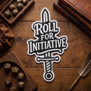 May include: A black and white embroidered patch with the text "ROLL FOR INITIATIVE" in a stylized font, featuring a sword design. The patch is set against a wooden background, with dice and books visible.