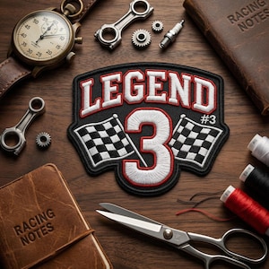 May include: A patch with the word "LEGEND" in white, outlined in red, and the number "3" with checkered flags. A vintage chronograph watch with a brown leather strap, along with other racing-themed items, are arranged on a wooden surface.