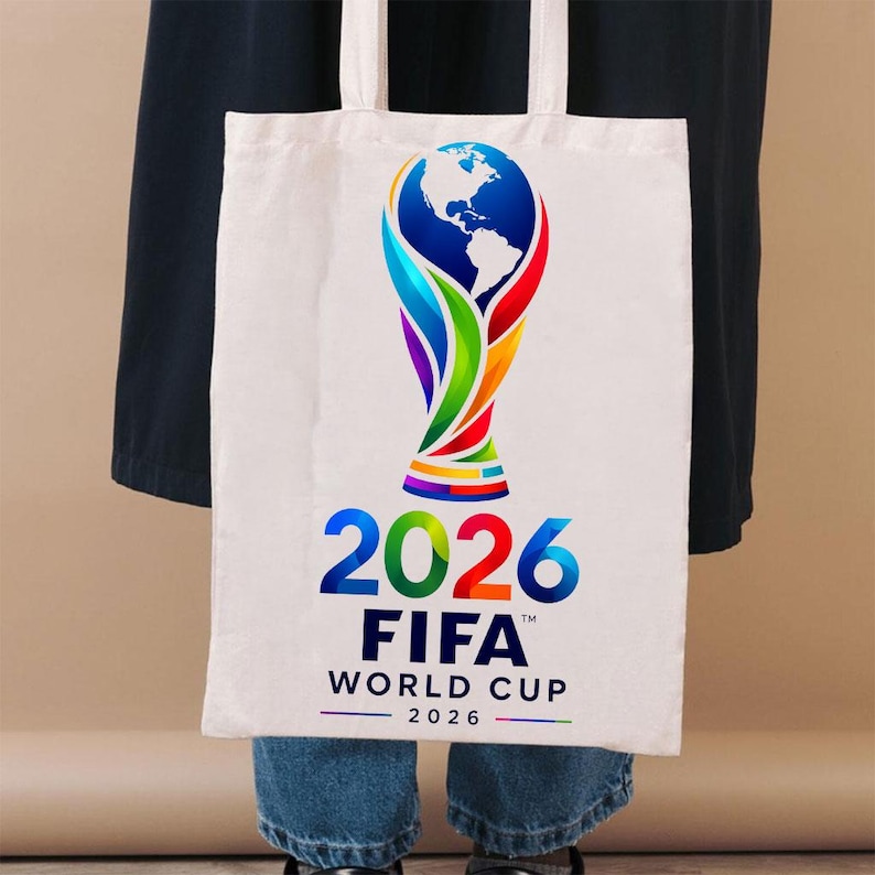 May include: A white canvas tote bag featuring a colorful graphic of the FIFA World Cup 2026 trophy. The design includes a stylized globe at the top with vibrant red, green, blue, and yellow accents, followed by the text 2026 FIFA WORLD CUP 2026.