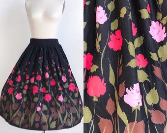 May include: A black, pleated skirt with a floral pattern. The skirt features pink and red flowers with green leaves and brown stems. The flowers are concentrated at the hem, creating a gradient effect.
