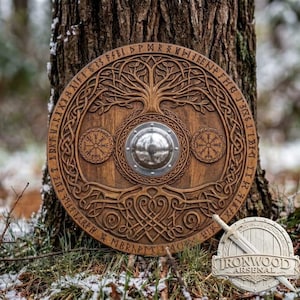 May include: A circular wooden shield featuring a central metal boss, intricate carved tree motifs, and two smaller circular symbols. The outer border displays runic inscriptions. A small logo with a sword and the text IRONWOOD ARSENAL is visible.