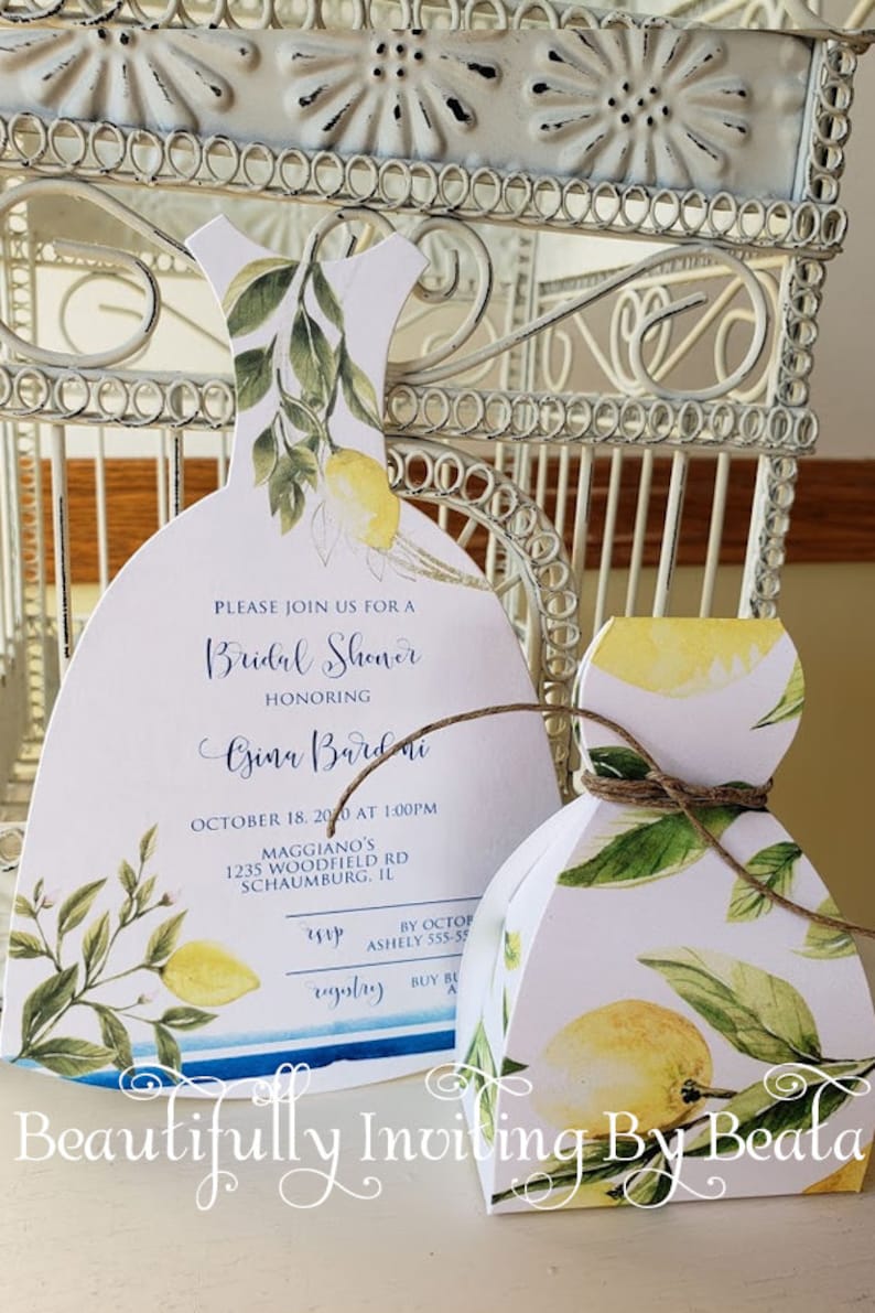 Puede incluir: Invitaci&oacute;n y caja de regalo para despedida de soltera blancas, ambas con forma de vestido, adornadas con limones y hojas verdes en acuarela. La invitaci&oacute;n incluye los detalles del evento. La caja de regalo est&aacute; atada con hilo. Las palabras "Beautifully Inviting By Beata" est&aacute;n escritas en la parte inferior.