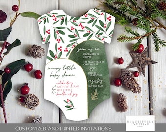 May include: A baby shower invitation in the shape of a onesie, featuring a white background with green leaves and red berries. The invitation includes the text "Merry Little Baby Shower" and event details. The design is accented with gold trim and decorative elements.