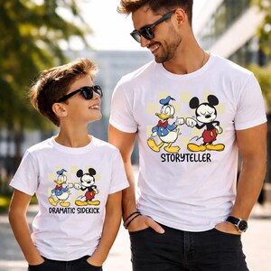 May include: White t-shirts featuring Donald Duck and Mickey Mouse fist-bumping. The shirt on the right says "Storyteller" and the shirt on the left says "Dramatic Sidekick". The shirts are worn by a man and a child.