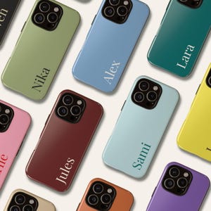 Op de afbeelding: Een verzameling kleurrijke telefoonhoesjes in verschillende tinten, waaronder groen, blauw en rood. Elke hoes heeft een naam in een contrasterende kleur. De hoesjes zijn in een verspreid patroon gerangschikt, waarbij hun verschillende kleuren en ontwerpen worden getoond.