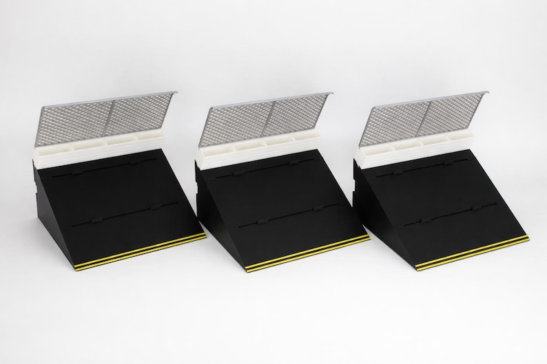 May include: Three black display stands with a white top section and a silver mesh cover. Each stand has a yellow stripe along the bottom edge. The stands are angled, creating a tiered display.