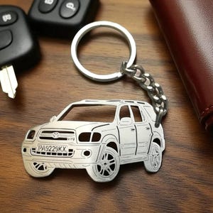 May include: Silver-colored SUV keychain with a key ring and chain. The keychain features a detailed outline of a vehicle, including the license plate. Car keys and a wallet are in the background.