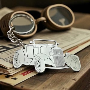 May include: A silver car-shaped keyring with a chain, placed on a stack of vintage papers. The keyring is a detailed outline of a classic car. Goggles with a circular lens are in the background.