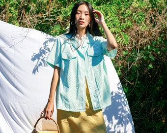 Può includere: Una donna indossa una camicia a quadri blu chiaro e bianco con una gonna gialla e una borsa di vimini.