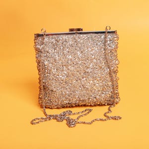 May include: A silver sequined evening bag with a chain strap. The bag is closed with a metal clasp.