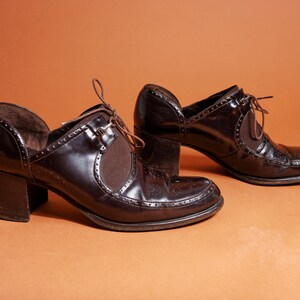 Pu&ograve; includere: Un paio di scarpe marroni in pelle con tacco, lacci sul davanti e cuciture decorative. Le scarpe hanno un tacco spesso e una punta a punta.