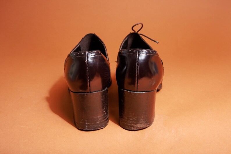 Pu&ograve; includere: Un paio di scarpe con tacco in pelle marrone con punta a punta e design con lacci. Le scarpe hanno un tacco spesso e una finitura lucida.