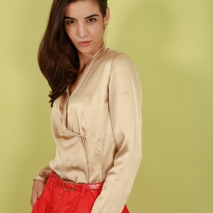 May include: A woman wearing a beige satin blouse with a red skirt and a brown belt. The skirt has a gathered design and buttons down the front.