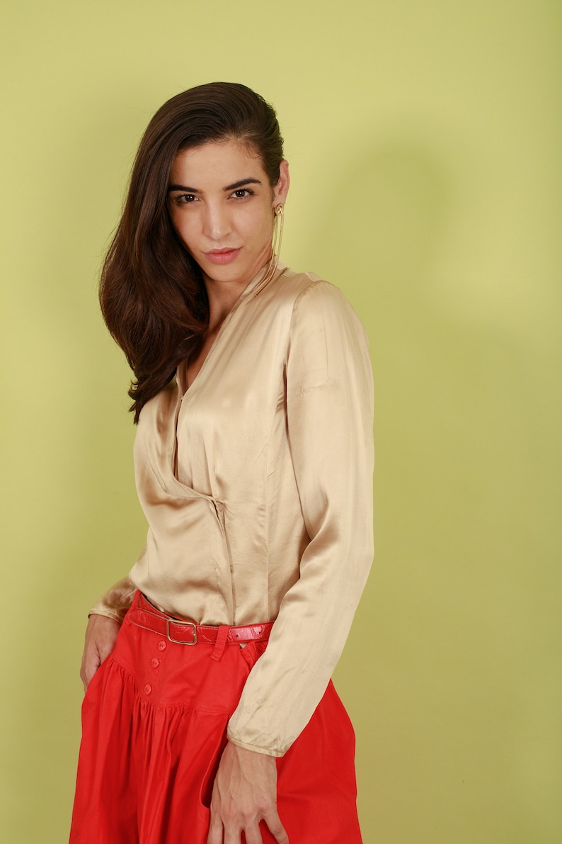 May include: A woman wearing a beige satin blouse with a red skirt and a brown belt. The skirt has a gathered design and buttons down the front.