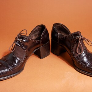 Pu&ograve; includere: Un paio di scarpe marroni in pelle con tacco e chiusura con lacci. Le scarpe hanno un design brogue e una punta a punta.