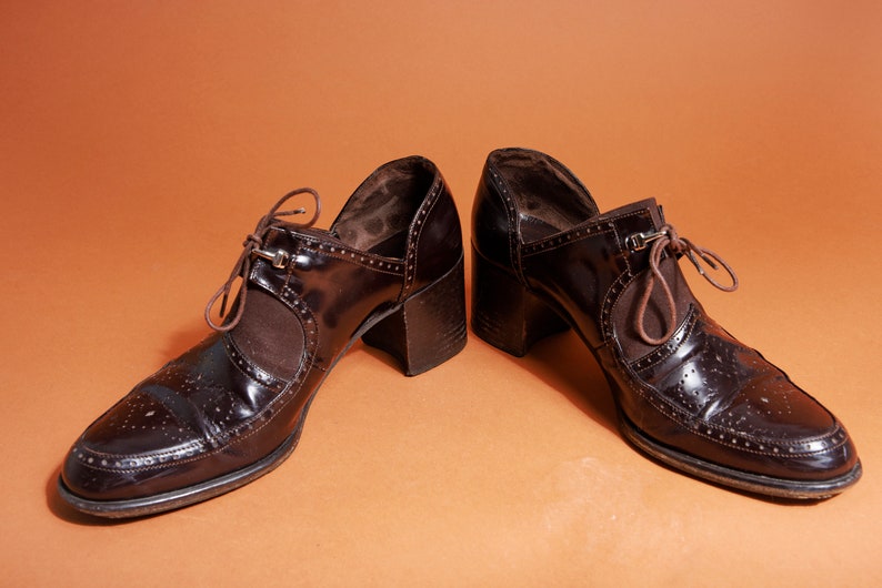 Pu&ograve; includere: Un paio di scarpe marroni in pelle con tacco e chiusura con lacci. Le scarpe hanno un design brogue e una punta a punta.