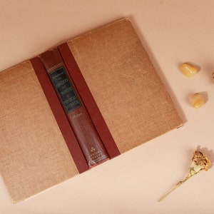 K&ouml;nnte beinhalten: Ein geschlossenes Buch mit einem braunen Leinenbezug und einem roten R&uuml;cken. Der R&uuml;cken tr&auml;gt den Titel "Concepts of Theories in Physical Science" und den Namen des Autors "Melvin". Das Buch liegt auf einer hellbraunen Oberfl&auml;che mit zwei kleinen gelben Steinen und zwei getrockneten Nelken.