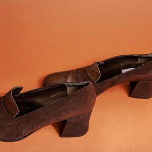 May include: A pair of brown suede heeled shoes with a contrasting brown leather toe cap. The shoes have a chunky block heel.