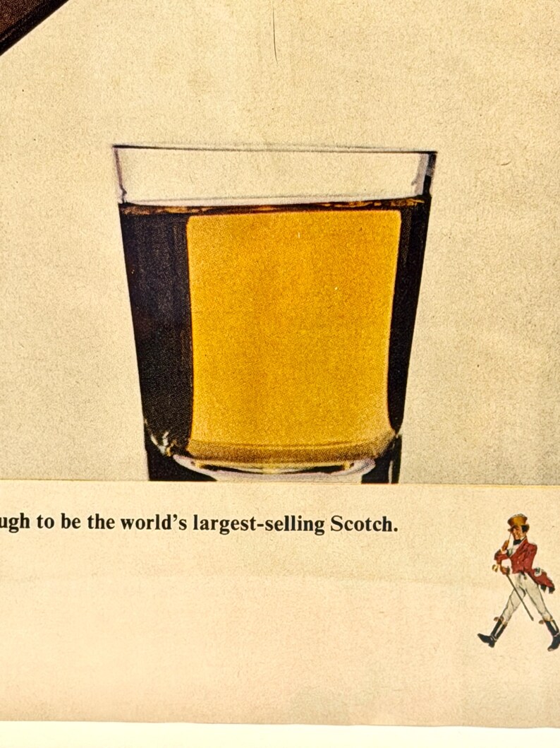 May include: A clear glass filled with amber liquid, likely a spirit, is the focal point. The image is an advertisement, with the text "...to be the world's largest-selling Scotch." A small illustration of a man in a red coat and black boots is also present.
