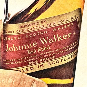 May include: Close-up of a vintage Johnnie Walker Red Label Scotch Whisky bottle. The label is red and gold with the brand name prominently displayed. The bottle is held by a hand, showcasing the classic design and branding.