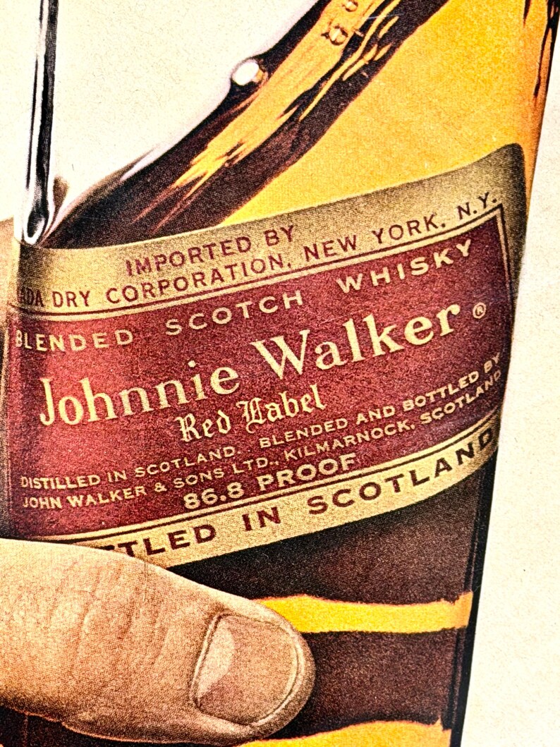 May include: Close-up of a vintage Johnnie Walker Red Label Scotch Whisky bottle. The label is red and gold with the brand name prominently displayed. The bottle is held by a hand, showcasing the classic design and branding.