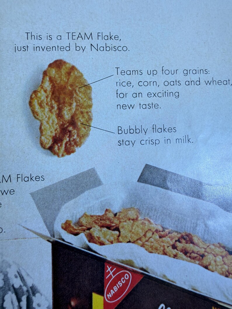 May include: An advertisement for TEAM Flakes cereal by Nabisco. The image shows a close-up of a single, bubbly flake and a box filled with flakes. Text highlights the cereal's ingredients: rice, corn, oats, and wheat.