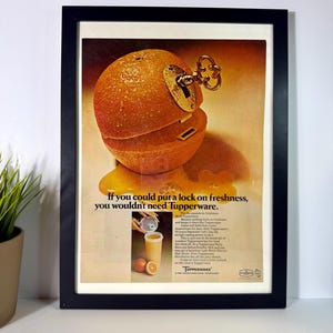 May include: Framed vintage Tupperware advertisement. The image features a cut orange with a key lock, with the text "If you could put a lock on freshness, you wouldn't need Tupperware."